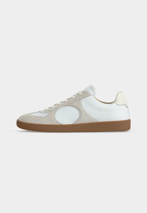 Low-profile casual sneaker met witte leren bovenkant, licht beige suède accenten, ronde neus, witte veters en rubberen zool.