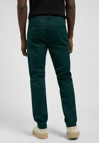 Chinos verdi in cotone con vestibilità slim, dotati di tasche posteriori e una texture liscia, abbinati a scarpe di colore chiaro.