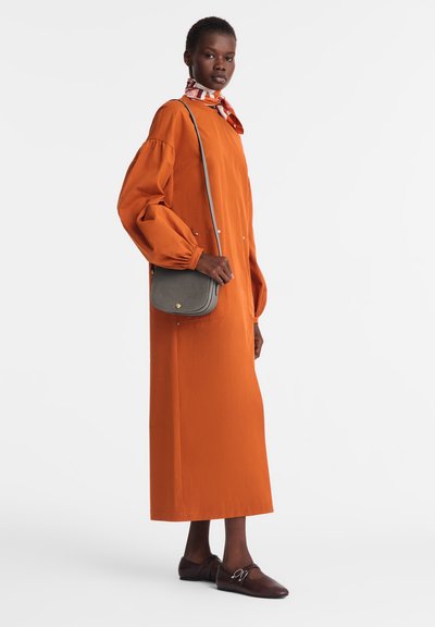 Langes oranges Kleid mit puffärmel, zwei Vorderaschen, kombiniert mit einer grauen Umhängetasche und braunen flachen Schuhen. Seiden-Schal mit Muster.