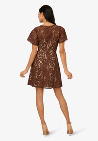 Robe en dentelle marron avec des manches courtes, un corsage ajusté et une jupe évasée. Motif floral délicat et texture transparente, avec une fermeture éclair dissimulée à l'arrière.