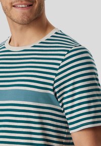Short-sleeve striped t-shirt featuring teal and beige horizontal stripes, with a solid teal panel across the chest and a round neckline.