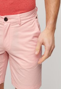 Pantalones cortos de color rosa claro hechos de tela de algodón, con cierre de botón, bolsillos frontales y una textura suave.