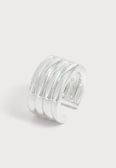 Un bracelet manchette argenté brillant avec plusieurs bandes courbes en relief, présenté sur un fond clair uni.