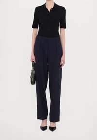 Czarny top z krótkim rękawem, granatowe spodnie z wysokim stanem, czarne szpilki w szpic oraz mała torebka w ciemnozielonym kolorze o fakturze. Czysty, dopasowany wygląd.