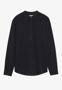 Chemise noire à manches longues avec col rond, patte de boutonnage à trois boutons et poche poitrine à gauche, présentée sur un fond uni.