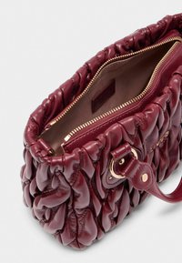 Bordeaux leren tas met een gequiltte textuur en een gouden rits. Interieur is bruin met een merklabel. Verstelbare schouderriem met metalen beslag.
