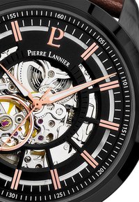 Reloj de pulsera analógico con caja de metal negro, esfera transparente, acentos en tono dorado, marcadores de horas en color rosa y correa de cuero marrón.