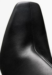 Scarpa di pelle nera con punta affusolata e finitura liscia opaca. Presenta una cucitura pulita lungo il bordo e un design elegante e moderno.