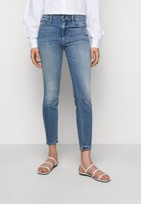 Sinisiä farkkuhousuja, joissa on vaalea pesu; viisi taskua, vetoketju eteen ja minimaalinen haalistuminen. Yhdistetty valkoisiin nauhakenkiin.