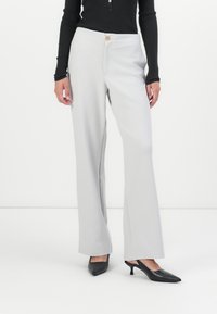 Pantalons gris à jambes larges avec une fermeture à bouton à la taille, texture lisse, associés à des escarpins noirs à talons ouverts.