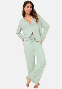 Vaaleanvihreä pyjama-setti, joka on valmistettu pehmeästä kankaasta; sisältää napitettava yläosa, jossa on kaulus ja pitsikoristeet housujen helmassa.
