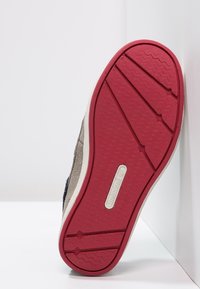 Suela de zapatilla de goma con una base texturizada en rojo. La parte superior combina ante azul oscuro con material beige claro. Área delantera reforzada.