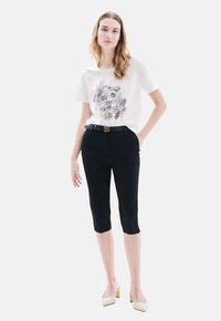 Pantalones negros cortos, de diseño ajustado, con un cinturón texturizado que presenta una hebilla dorada. Combinados con una camiseta blanca con acentos de estampado floral.