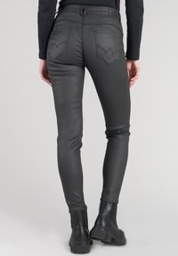Jeans skinny in faux leather neri con vita alta, dotati di tasche posteriori con un motivo di cucitura decorativo. Texture liscia e vestibilità aderente.
