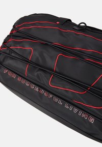 Sac en tissu noir avec des coutures rouges et le texte "POUR UNE VIE RÉUSSIE." Conçu avec des compartiments et une texture lisse.