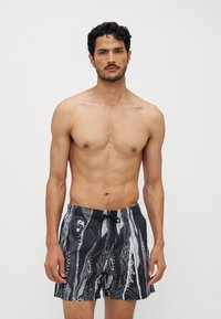 Shorts de bain à motif noir et blanc avec une taille élastique, un cordon de serrage et une coupe confortable. Le tissu semble léger et texturé.