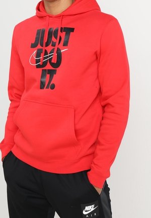 Hoodie rouge avec une poche kangourou et une capuche à cordon de serrage, arborant un audacieux graphisme noir "JUST DO IT." et le logo Nike. Texture de tissu douce.