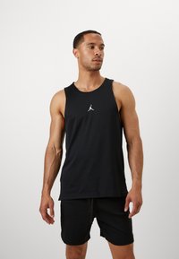 Débardeur de sport sans manches noir avec texture respirante, arborant un logo Jumpman blanc sur la poitrine, associé à un short noir.