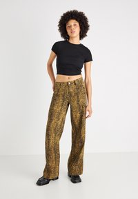 Pantalone širokog kroja s uzorkom zmijskog printa u zlatnim i smeškim tonovima, s visokim strukom, teksturiranom tkaninom i jednim dugmetom sprijeda. Crni kratki top.
