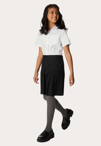 Camicetta bianca a maniche corte con tasca, gonna nera plissettata, collant grigi e scarpe nere slip-on con suola spessa.
