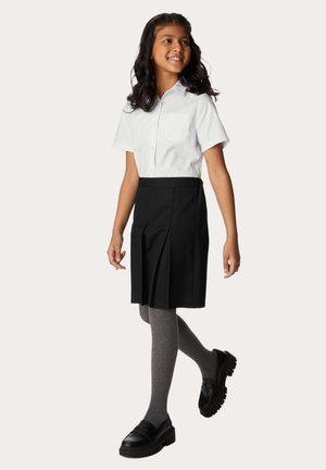 Camicetta bianca a maniche corte con tasca, gonna nera plissettata, collant grigi e scarpe nere slip-on con suola spessa.