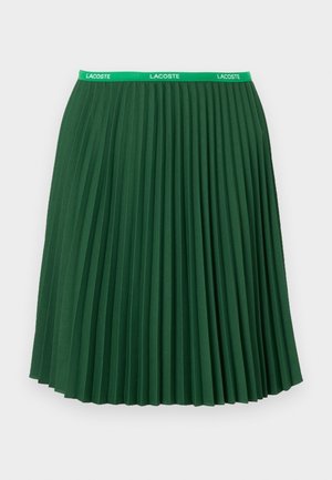 Gonna plissettata verde realizzata in tessuto con una consistenza liscia; presenta un elastico in vita con il logo Lacoste verde e arriva fino a metà polpaccio.