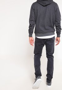 Felpa con cappuccio grigia scura, dotata di tasca a marsupio, abbinata a jeans neri e sneakers grigie. L'outfit presenta una vestibilità comoda e un design informale.