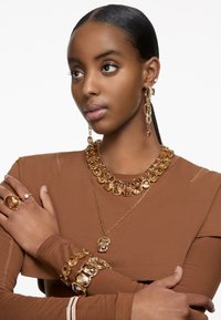 I gioielli color oro presentano grandi pietre sfaccettate, tra cui una collana massiccia, orecchini pendenti e un braccialetto. Finitura liscia e lucida.