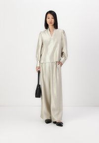Blusa di satin argentato con maniche a sbuffo, abbinata a pantaloni larghi coordinati. Il modello tiene una borsa nera e indossa scarpe basse nere.