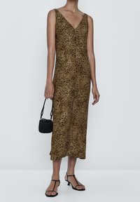Robe midi marron à pois avec un décolleté en V profond et sans manches. Tissu texturé, associée à un sac tissé noir et des sandales à lanières.