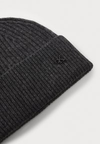Black knitted beanie with a ribbed texture, featuring a folded cuff and a small metal logo tag sewn onto the cuff.