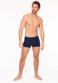 Boxers bleu marine avec un motif à pois, une taille élastique et une coupe ajustée, présentés par un modèle masculin sur un fond clair.