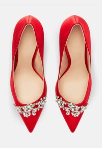 Crvene satenaste balerinke s oštrim nosom, sa dekorativnim skupom prozirnih dragulja sprijeda. Glatka tekstura i nisko izrezani bokovi.