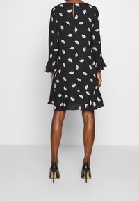 Svart klänning med vit bladtryck, långa ärmar med utsvängda manschetter, volangad fåll och nyckelhål i ryggen. Bärs med svarta högklackade skor.