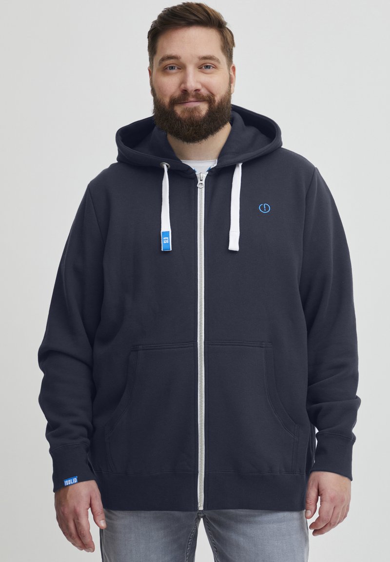 Mornarica zip-up dukserica izrađena od mekog materijala, s bijelim vezicama, kenguru džepovima i malim logotipom na prsima. Osvježeni rukavi u svijetloplavoj boji.