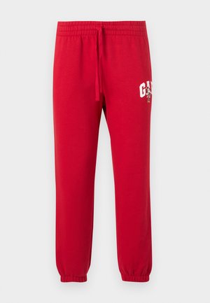 Pantalones deportivos rojos con puños elásticos, cintura con cordón y logotipo blanco "GAP" junto con un pequeño personaje de dibujos animados en el muslo izquierdo.