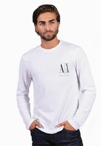 Long-sleeve white t-shirt with a black "AX" logo and "ARMANI EXCHANGE" text. The fabric appears soft, with a relaxed fit and round neckline.