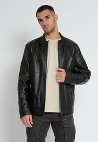 Schwarze Lederjacke mit einem Reißverschluss vorne, stehendem Kragen und zwei seitlichen Taschen. Glatte Textur mit Nahtdetails und einer lässigen Passform.