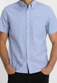 Camicia celeste a maniche corte con bottoni, realizzata in misto cotone, dotata di taschino sul petto, colletto a punta e bottoni bianchi in plastica.