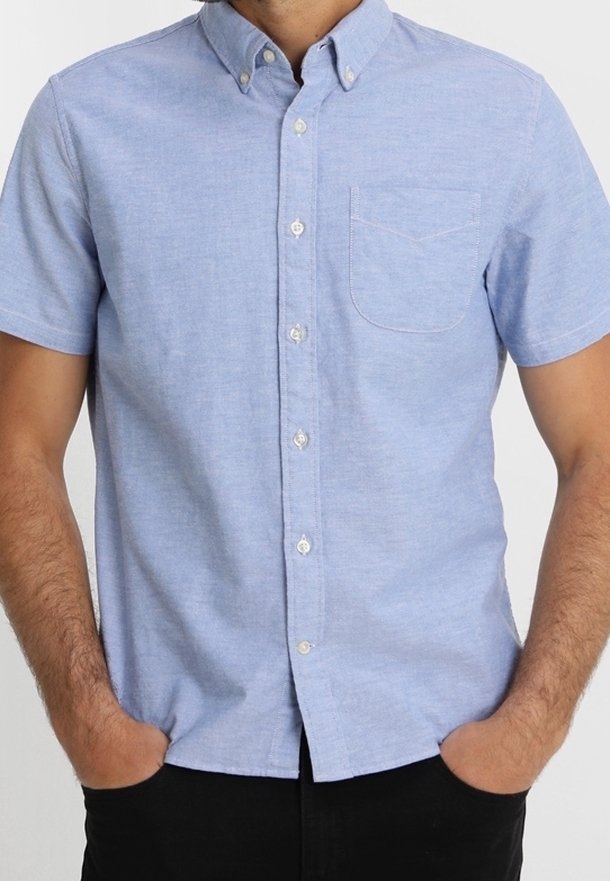 Camicia celeste a maniche corte con bottoni, realizzata in misto cotone, dotata di taschino sul petto, colletto a punta e bottoni bianchi in plastica.