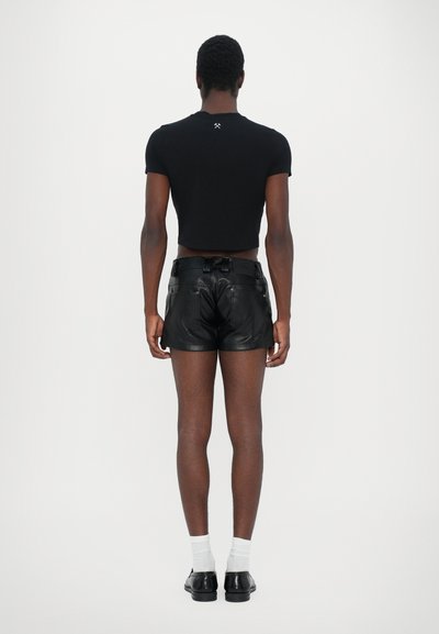 Schwarzes, cropped T-Shirt und schwarze Leder-Shorts, die eine glatte Textur zeigen. Auffällige Rückendetails und eine figurbetonte Passform mit einem sauberen Abschluss.