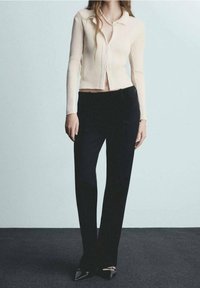 Kość słoniowa, prążkowany kardigan z kołnierzykiem i dopasowanym krojem, zestawiony z czarnymi, taliowanymi spodniami i czarnymi, czubkowatymi szpilkami.