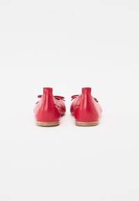 Ballerines en cuir rouge avec un motif matelassé, des bouts ronds et des nœuds décoratifs au talon. La semelle est beige et plate.