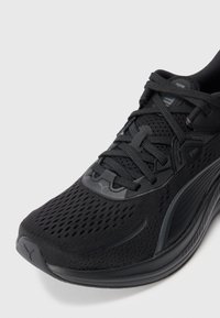 Schwarzer Sportschuh mit atmungsaktivem Mesh-Obermaterial, dicker gepolsterter Sohle und schwarzen Schnürsenkeln, die kreuzweise gebunden sind, auf weißem Hintergrund.