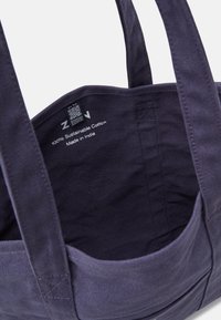 Sac en toile en coton de couleur bleu marine profond, avec des poignées robustes, une étiquette intérieure avec des instructions d'entretien, et un design simple et sans motif.