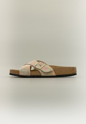 Beige slippersandalen met een kurken zool, zwart loopvlak, bloemmotief en een verstelbare goudkleurige gespriem over de bovenkant.