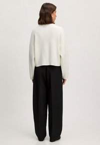 Witte cropped trui met ribbel textuur, voorzien van lange mouwen, gecombineerd met zwarte wijde broek. Minimalistisch ontwerp zonder zichtbare patronen.