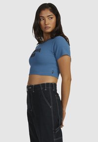 Blå cropped T-shirt lavet af ribbet stof med korteærmer og broderet tekst på forsiden, parret med højtaljede sorte bukser.