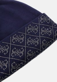 Granatowa dziana czapka z prążkowanym mankietem, z diamentowym wzorem wykonanym z metalowych ćwieków na końcu. Miękka tekstura i elastyczne dopasowanie.