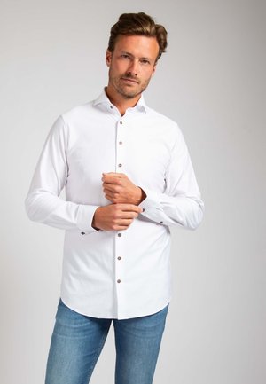 Witte overhemd met bruine knopen en lange mouwen, met een klassieke kraag en een gebogen zoom, gedragen met lichtblauwe jeans.